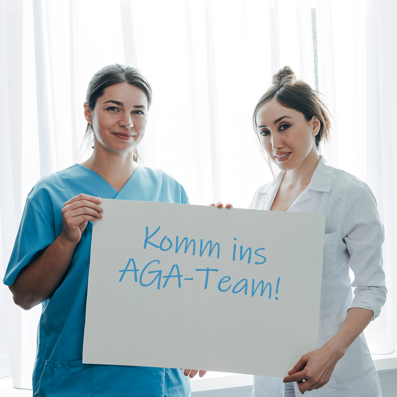 Pflegerinnen halten gemeinsam ein Schild hoch, mit der Aufschrift: "Komm ins Aga Team"